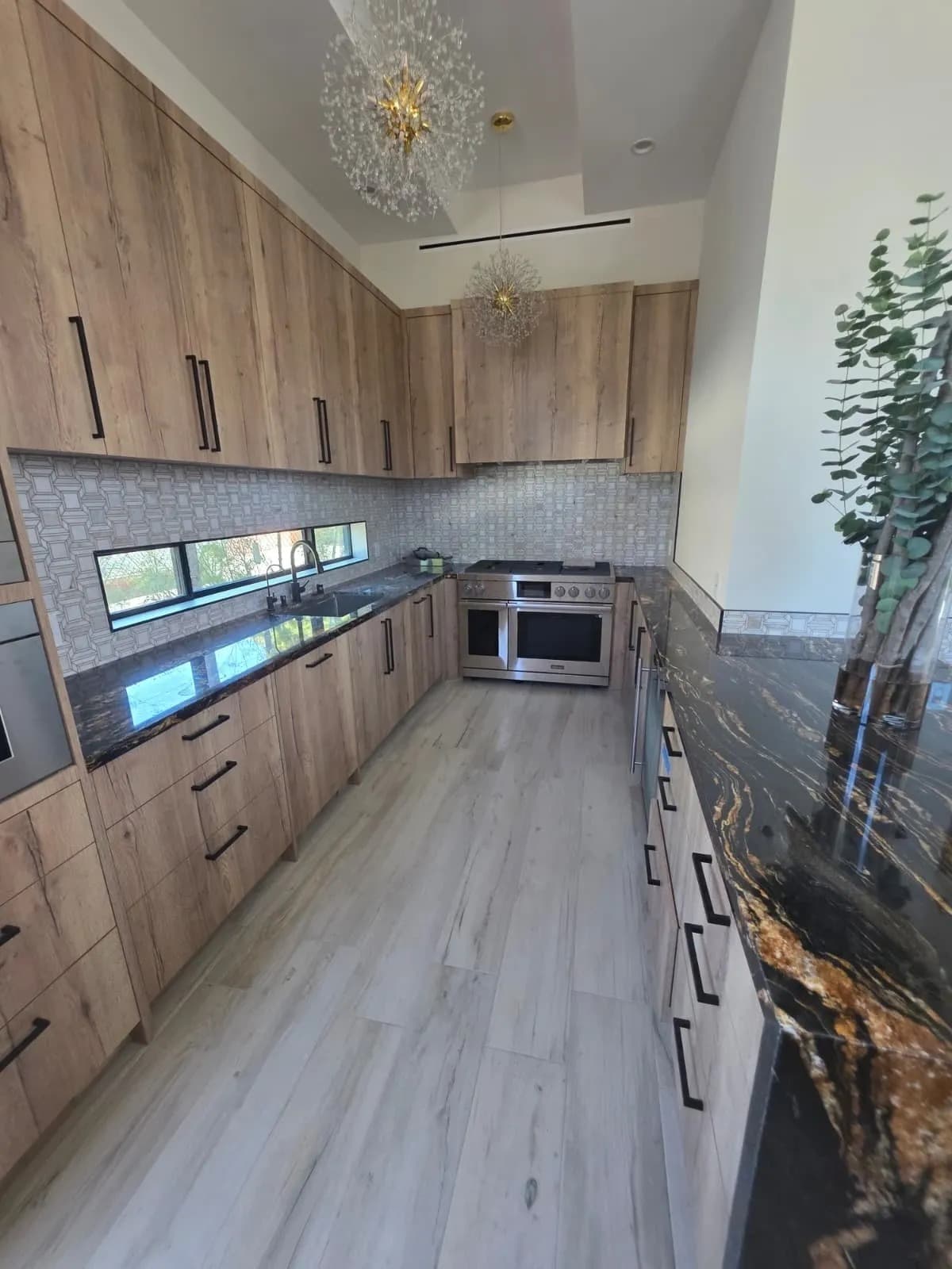 Luxury chef kitchen remodel in Lake Oswego OR with rift-sawn wood-grain cabinetry, exotic black-and-gold Nero Portoro granite countertops, Waterford starburst chandelier, geometric mosaic backsplash, and professional stainless range